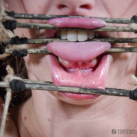 Bella Rossi is bound in wood with mouth spreader with clamps on her big tits